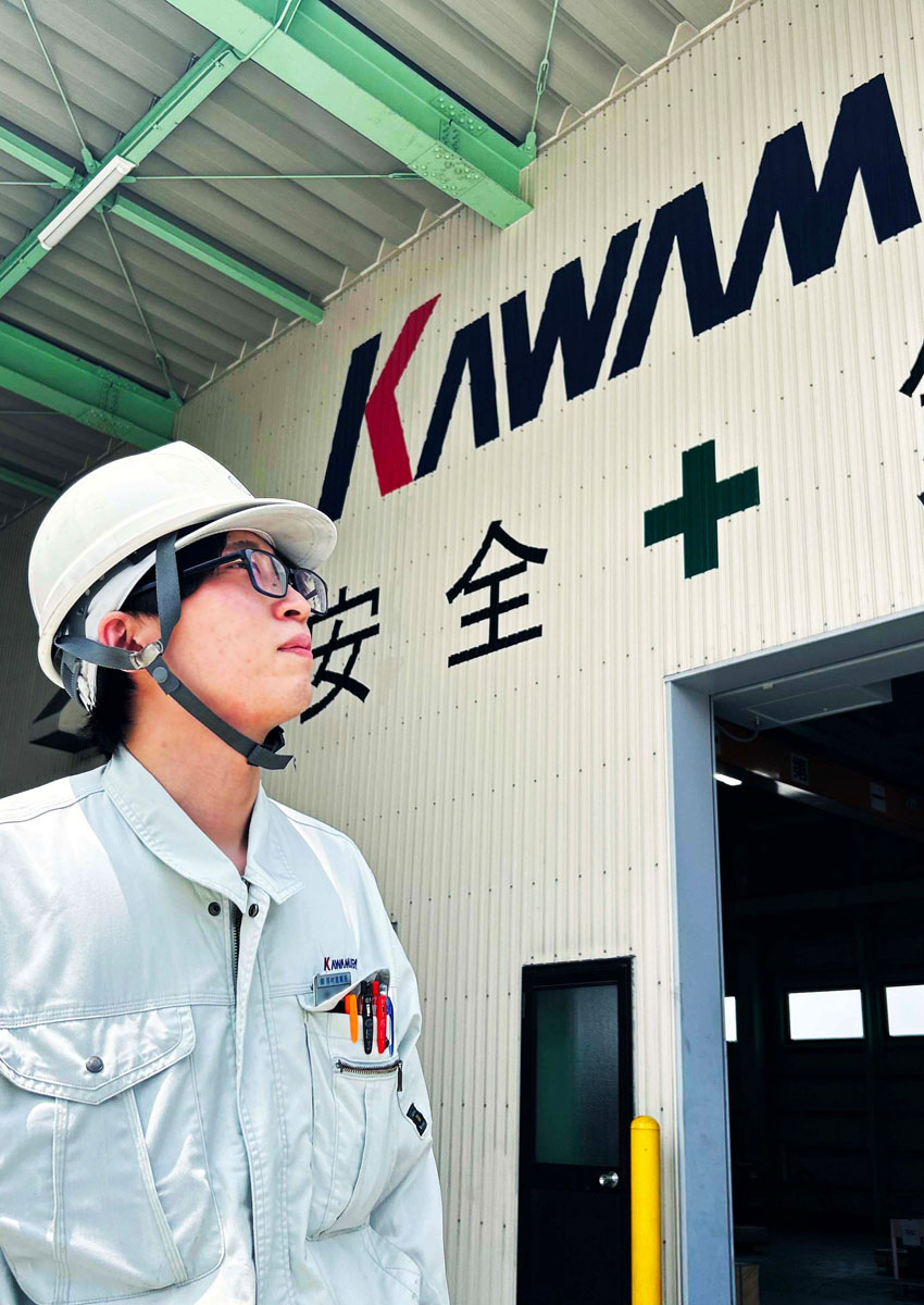 工場を背景に上を見上げる鉄工事業部の作業員