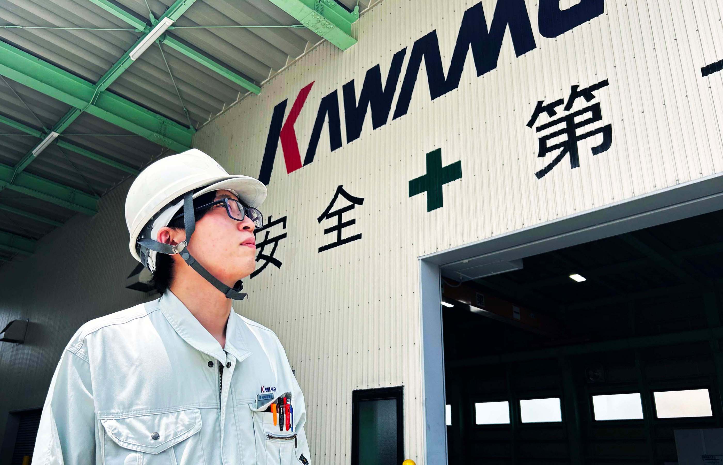 工場を背景に上を見上げる鉄工事業部の作業員