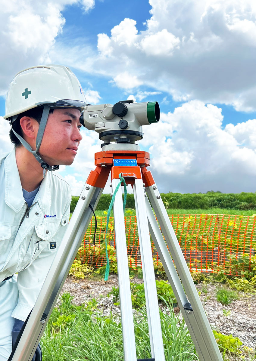 測量機器のレンズを覗く建設事業部の作業員